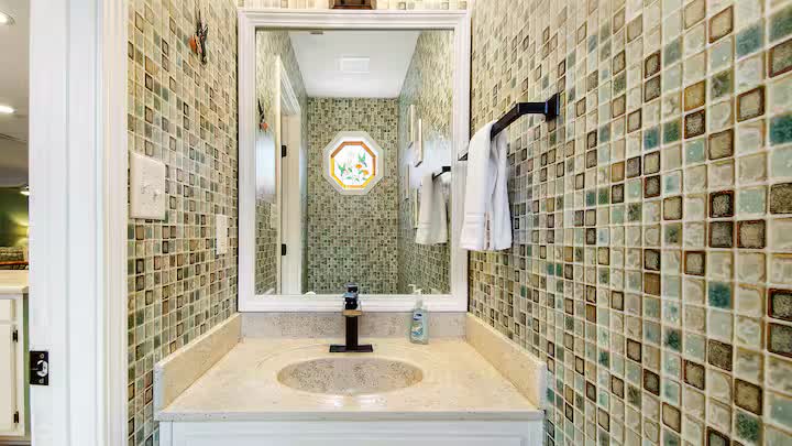 Bathroom vanity with mosaic tile walls and framed mirror
