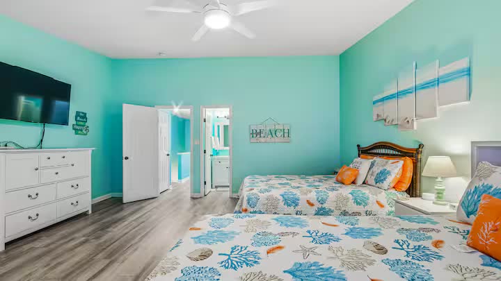 Bedroom with two queen beds in coral-print bedding, dresser, and wall-mounted TV