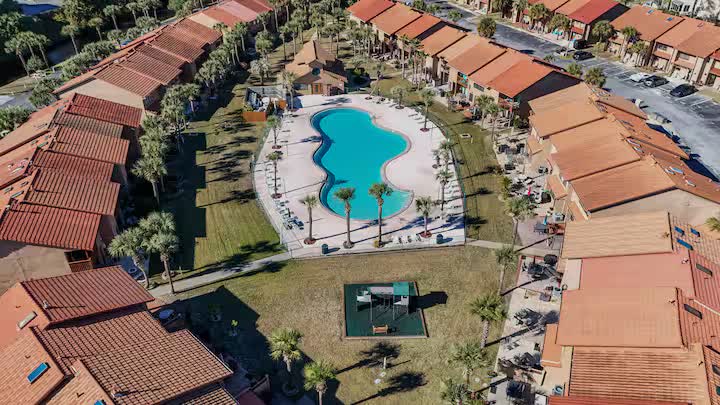 Aerial view of a resort pool surrounded by palm trees and townhomes